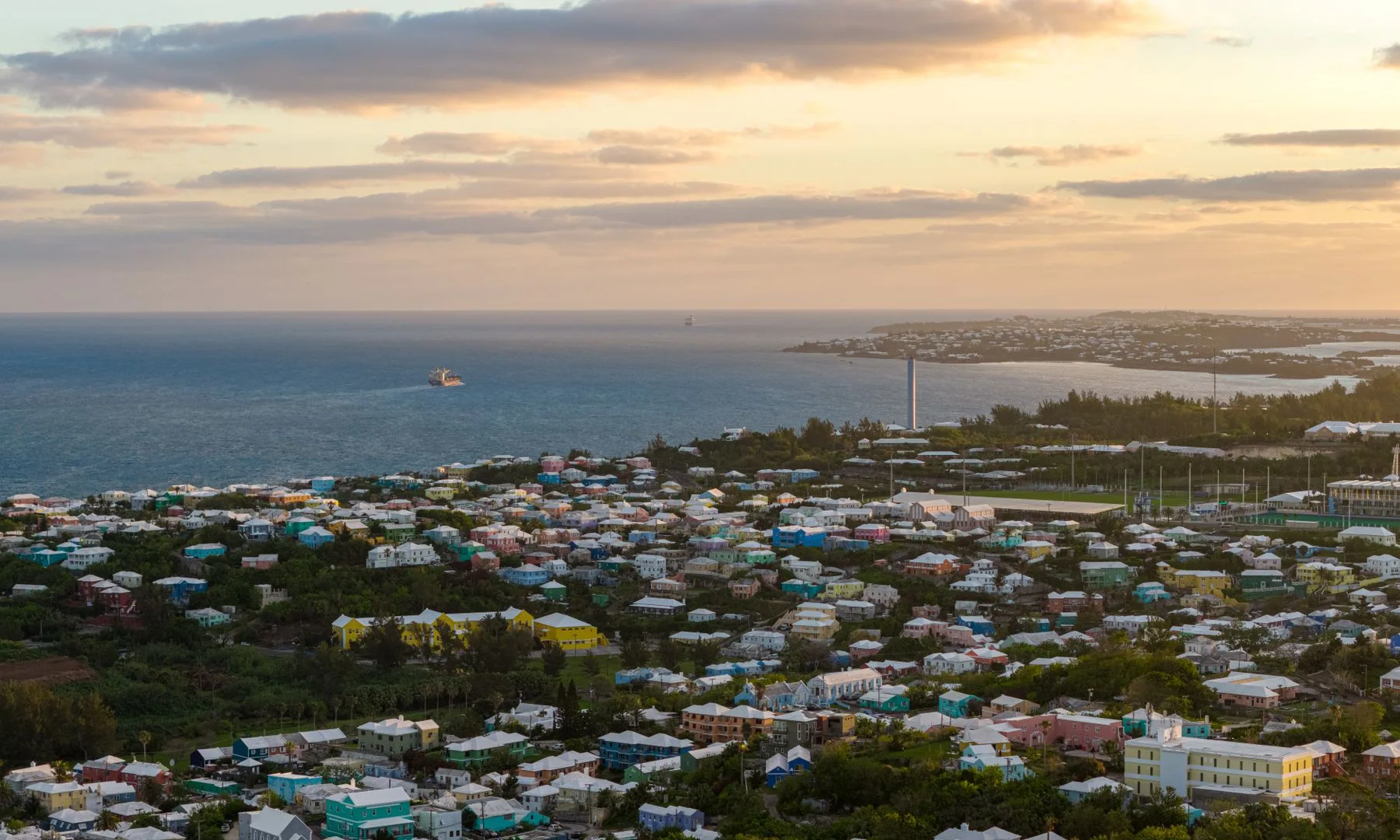 Stunning aerial view of Bermuda's coastal town with vibrant houses and ocean at sunset.