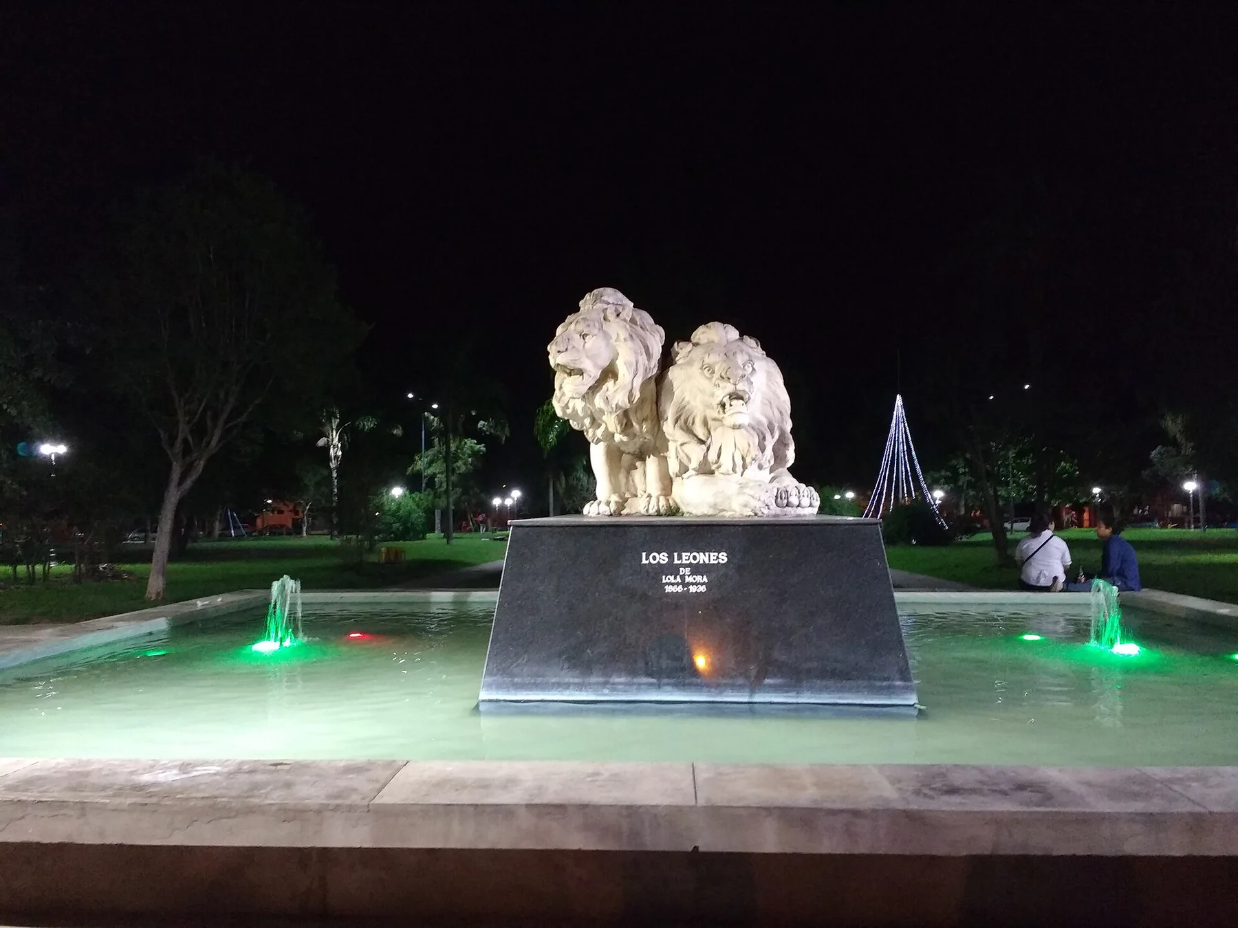 Vista nocturna de la fuente que alberga la escultura "Los Leones", obra de la artista argentina Lola Mora. La pieza se encuentra ubicada en la Plaza Hipólito Yrigoyen del barrio Ciudad de Nieva en San Salvador de Jujuy. Se observa la iluminación de la fuente y detalles de la escultura sobre su base de piedra.