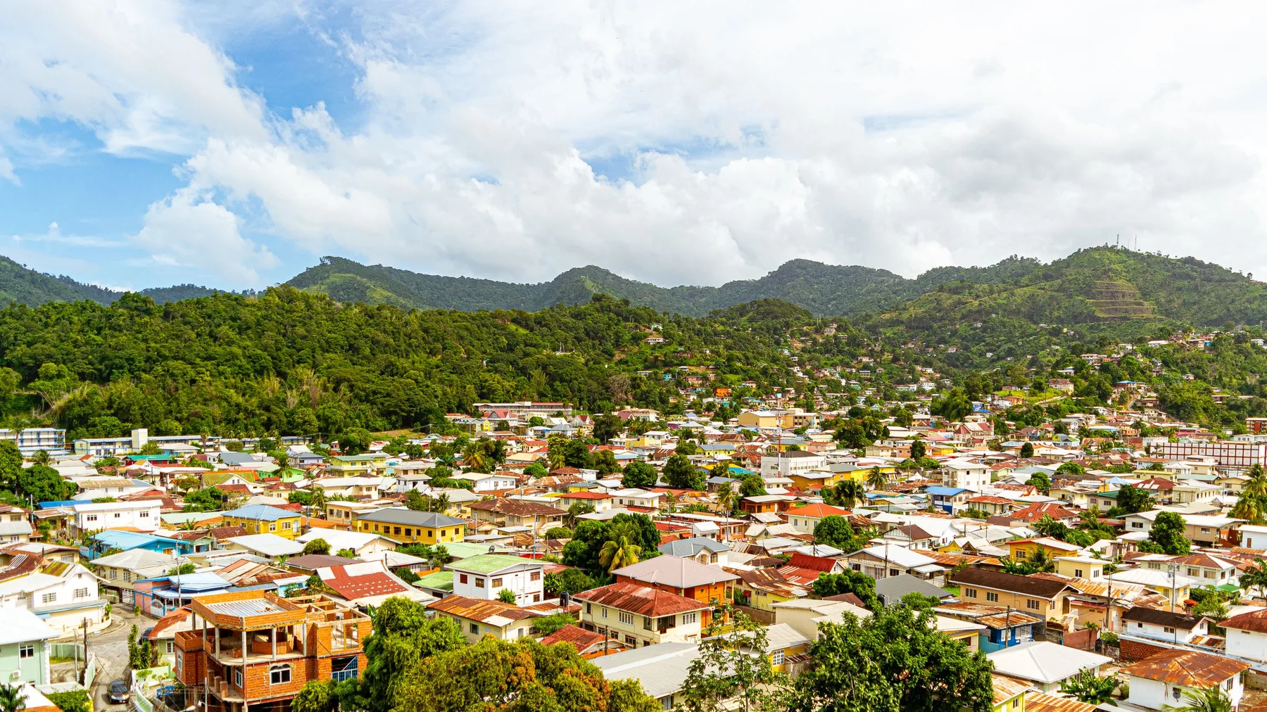 Vista aérea de Port of Spain con montañas verdes al fondo y cielo azul en Trinidad y Tobago
