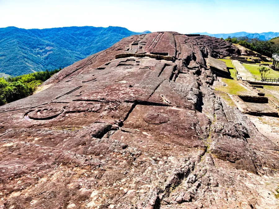 The archeological site of Samaipata Fort (elev. 1,900m/6,234ft) consists of the ceremonial center carved into a red sandstone rock and an administrative and residential district down the hill off to the right. The carvings in the rock include representations of animals, geometric shapes, niches, can