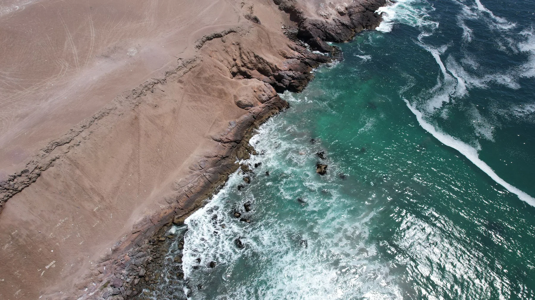Stunning aerial shot of rocky coastline meeting turquoise ocean waves in the Antofagasta region.