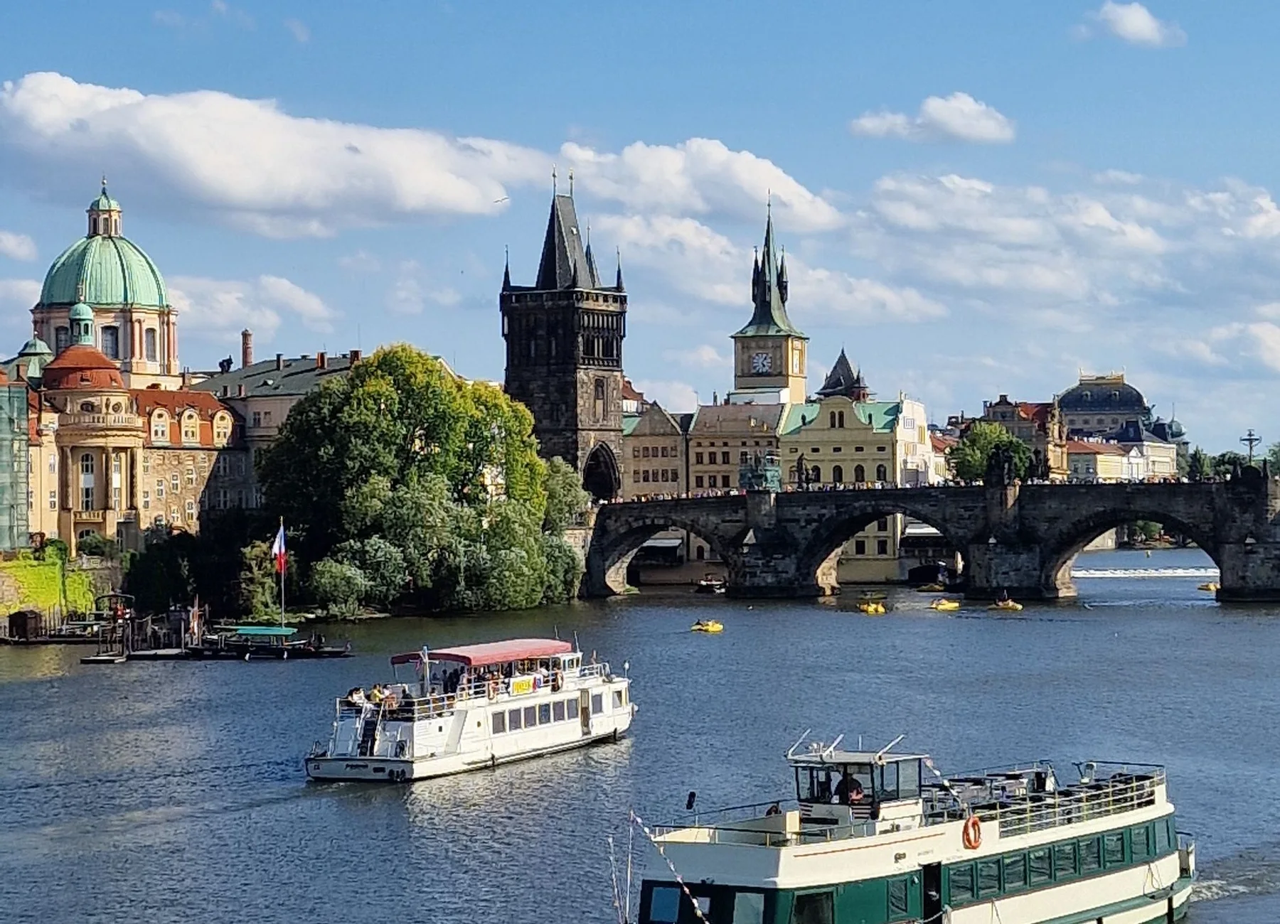Barcos navegando por el río Vltava con el puente Carlos y el perfil histórico de Praga al fondo