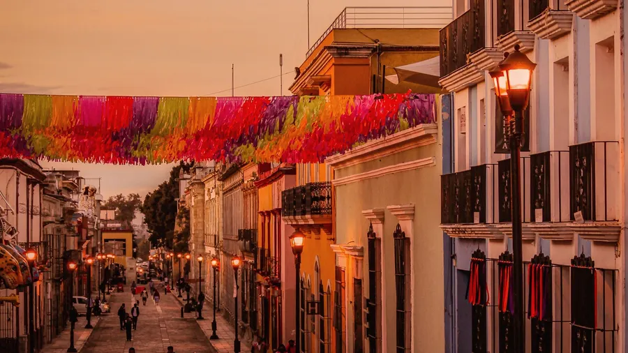 Colorful street scene in Oaxaca City featuring colonial buildings and festive decorations during sunset.