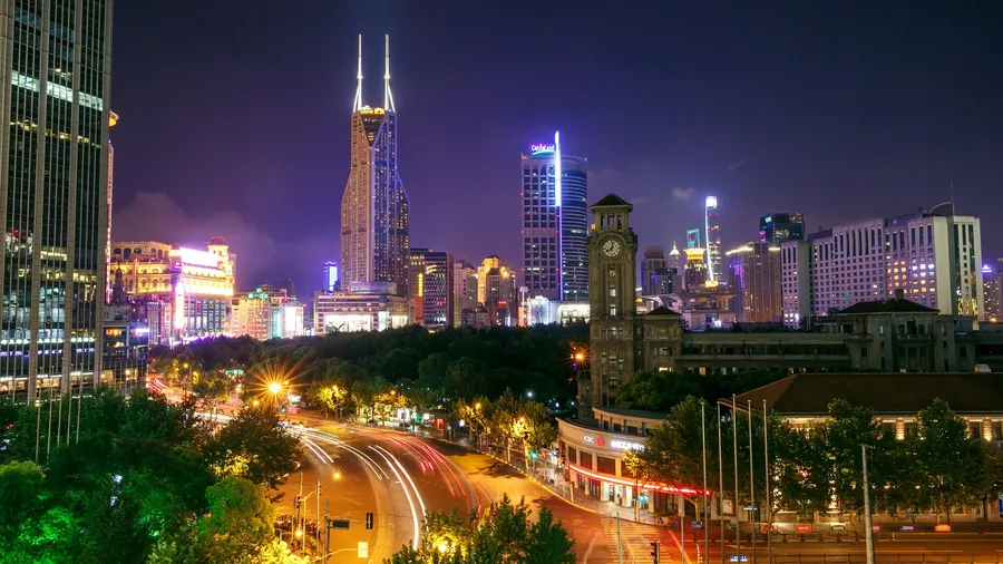 Panorámica nocturna de una ciudad con rascacielos iluminados y estelas de luces en las avenidas