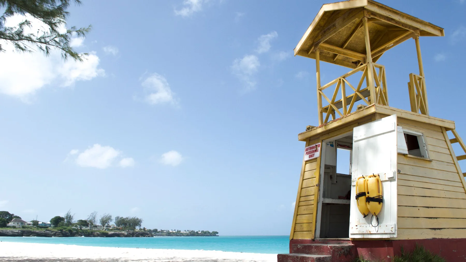 Torre de vigilancia de madera en una playa de Barbados, con cielo despejado y mar azul