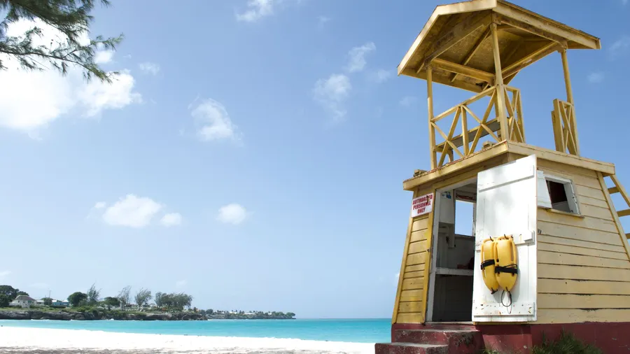 Torre de vigilancia de madera en una playa de Barbados, con cielo despejado y mar azul