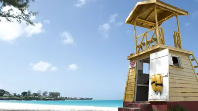Torre de vigilancia de madera en una playa de Barbados, con cielo despejado y mar azul