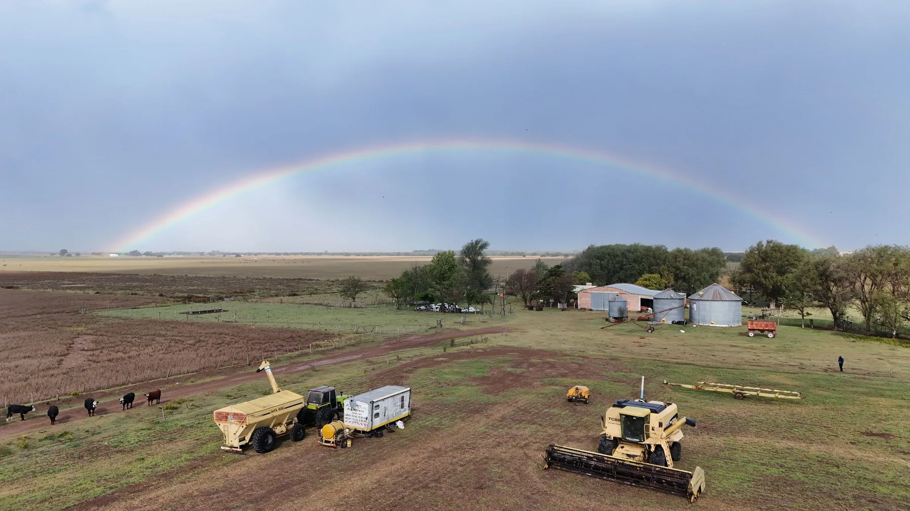 Arcoíris sobre un campo pampeano con maquinaria agrícola y galpones