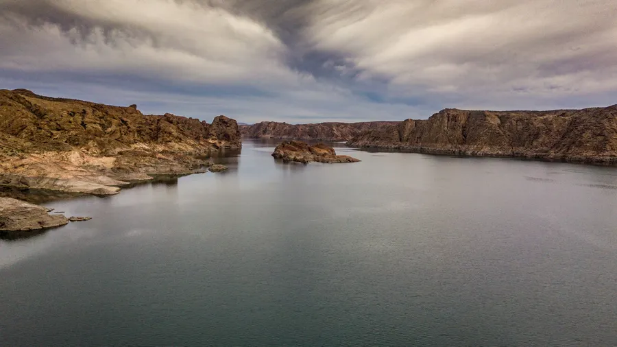 Lago calmo rodeado de paisajes rocosos bajo un cielo dramático en Trelew, Chubut, Argentina