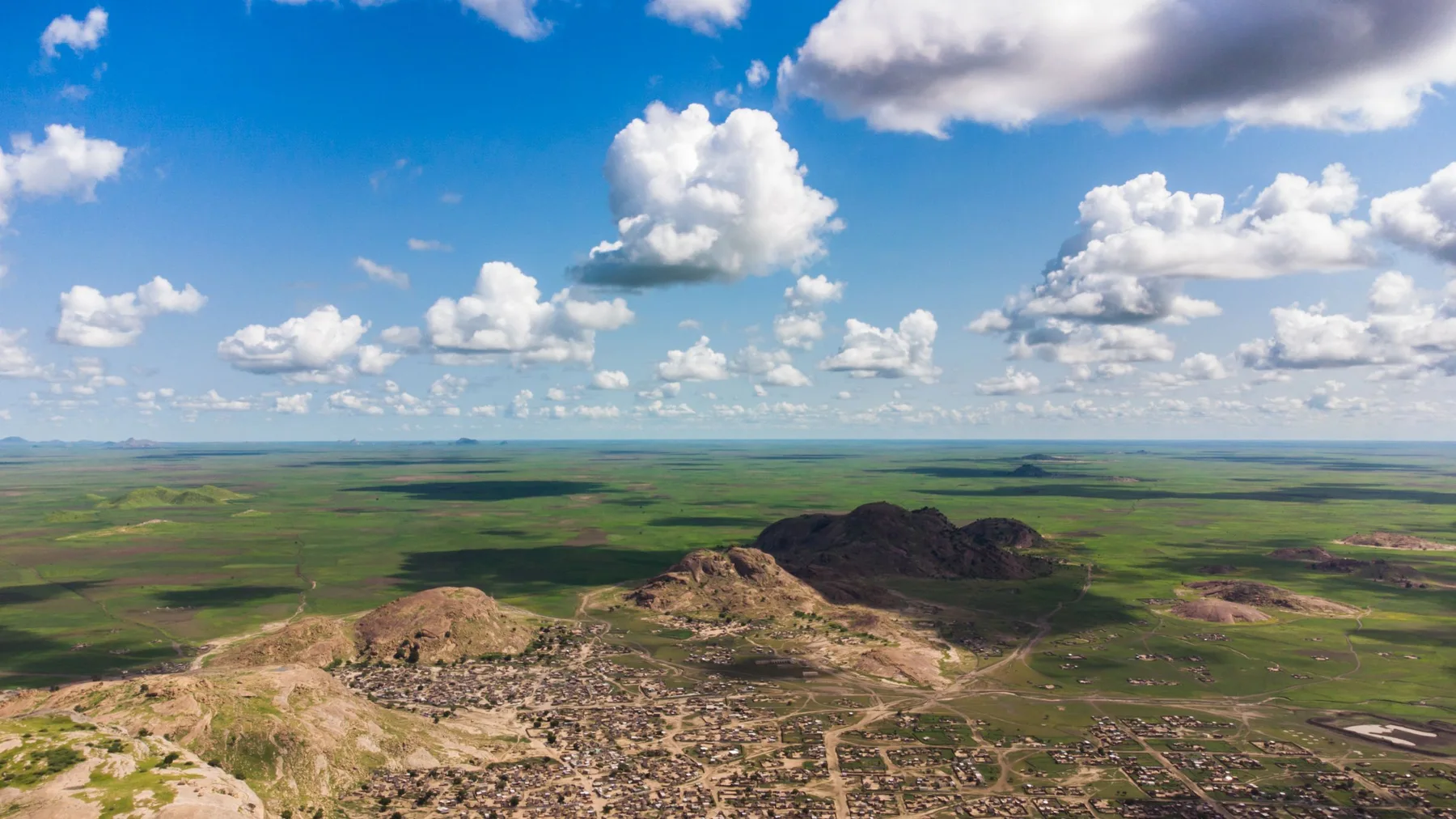Vista aérea de Baylah, Sudán, con colinas, campos y casas bajo un cielo azul con nubes