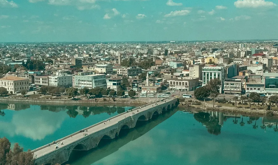 Vista aérea de una ciudad junto a un río, con un puente y cielo azul