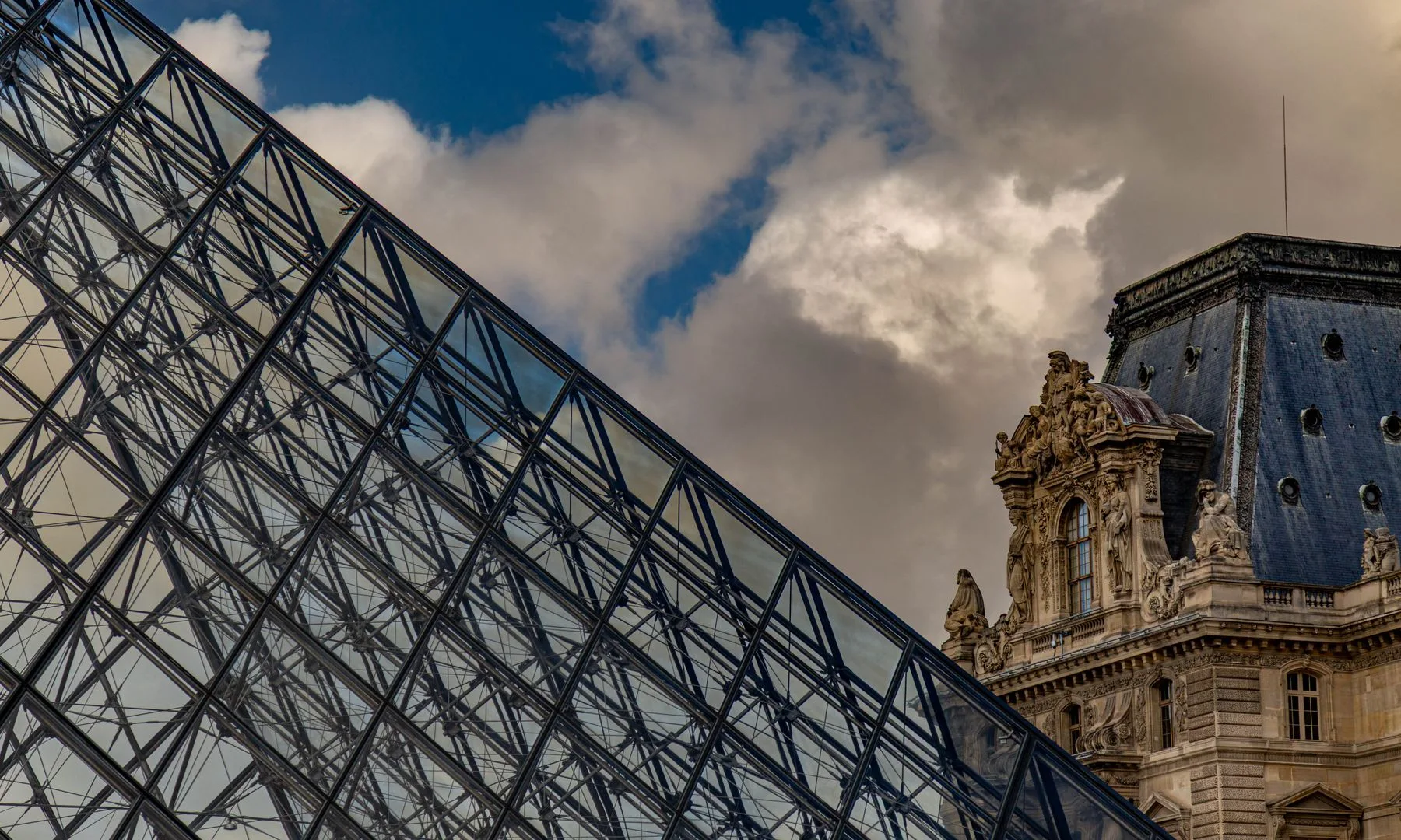 Iconic view of the Louvre Pyramid and ornate historic architecture in Paris, France.
