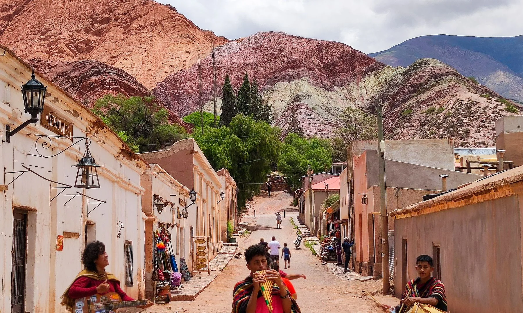 Músicos callejeros en Tilcara, Argentina, con cerros coloridos y arquitectura tradicional de adobe
