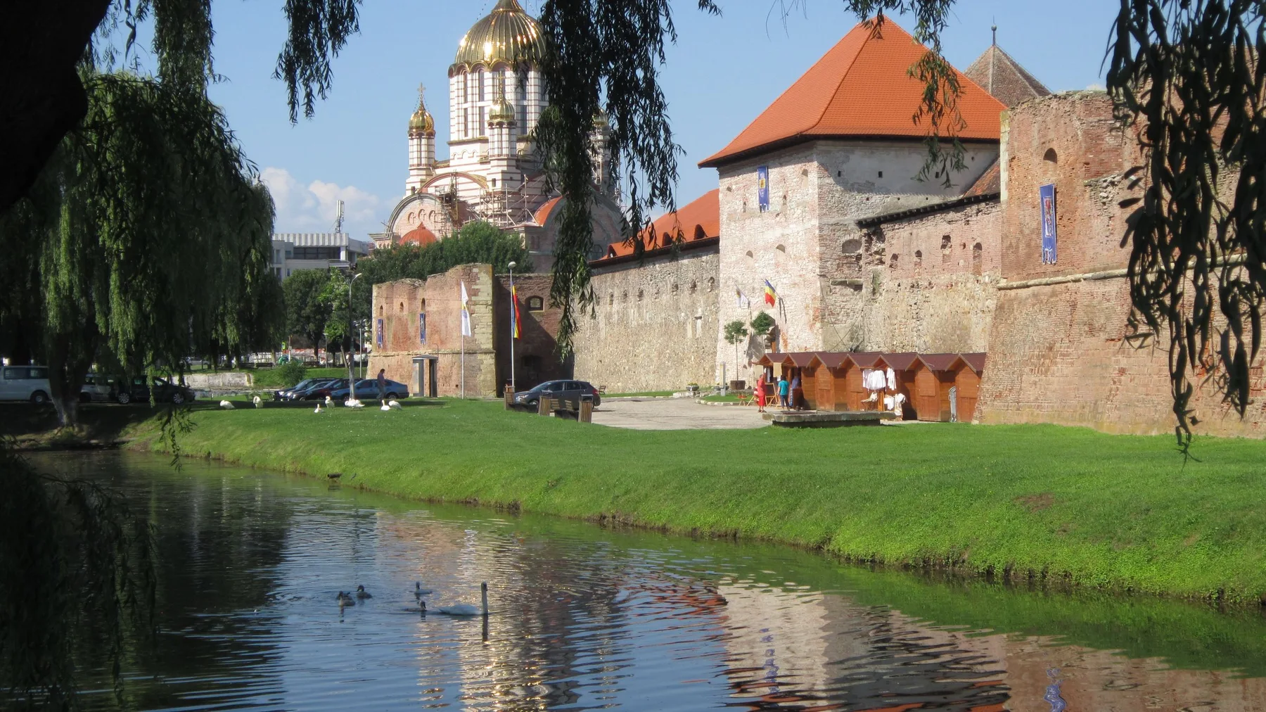Castillo de Făgăraș reflejado en el agua, con cisnes y ambiente sereno veraniego