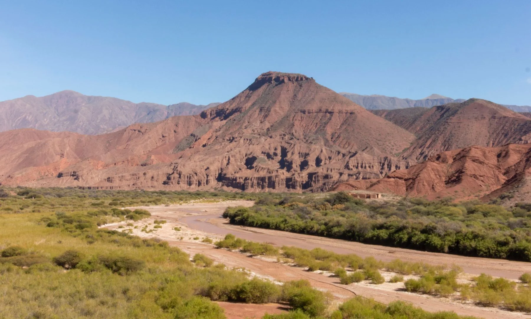Vista del valle de Cafayate con montañas escarpadas, vegetación abundante y cielo azul despejado