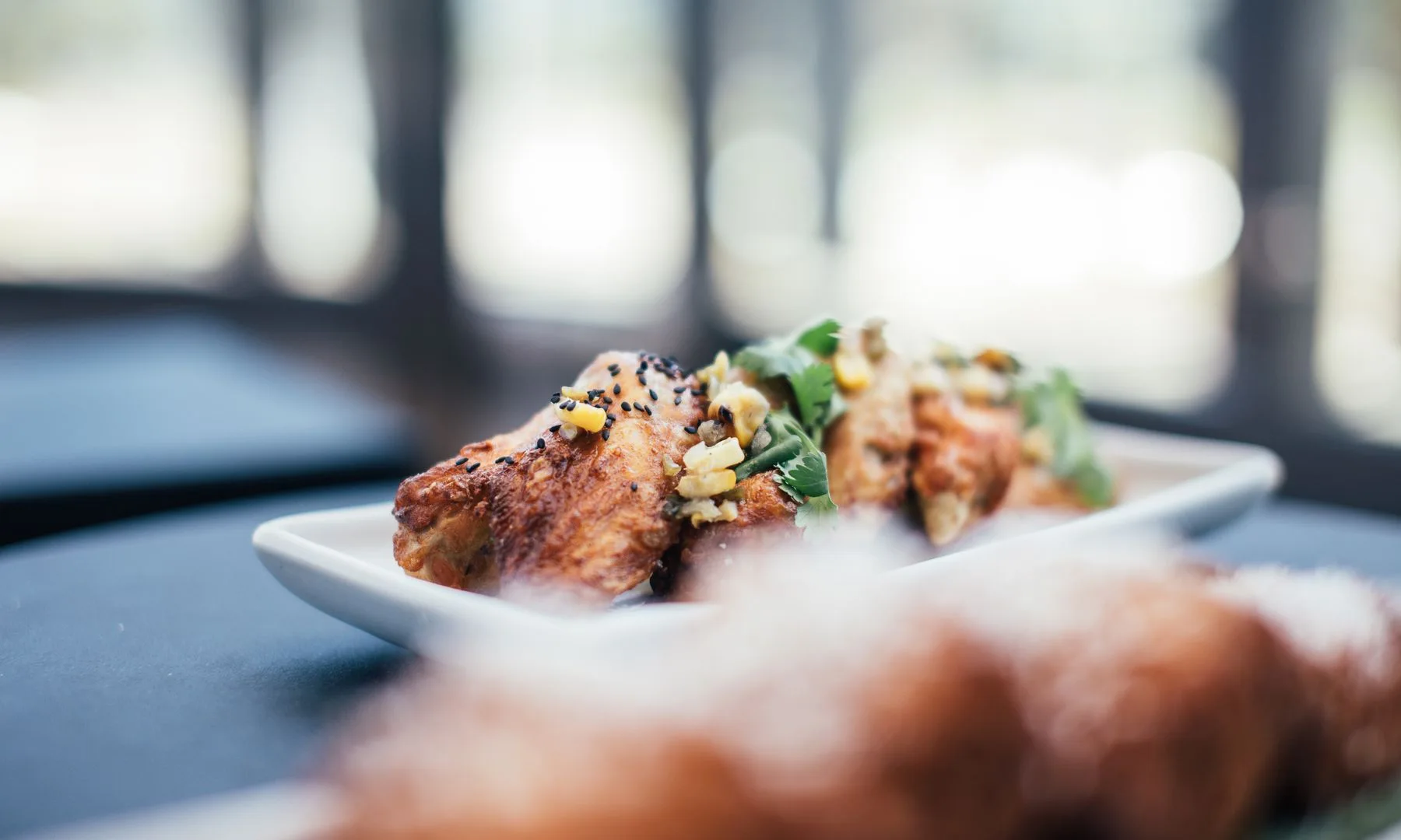 Appetizing roasted chicken wings decorated with parsley and corn served on white plate on table in restaurant on blurred background