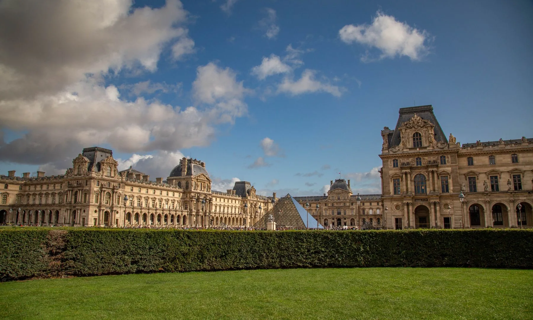 The Louvre Museum with its iconic Pyramid under a clear blue sky in Paris, France.