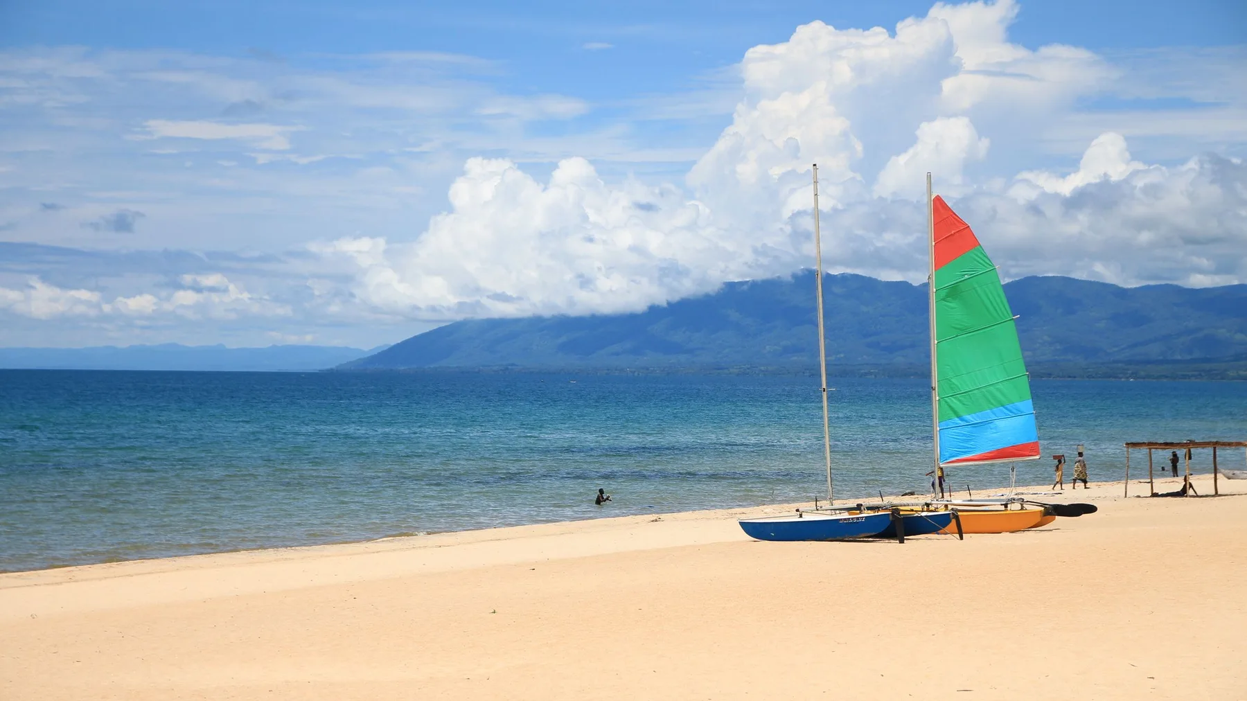 Velas coloridas sobre una playa soleada del lago Malaui con montañas al fondo