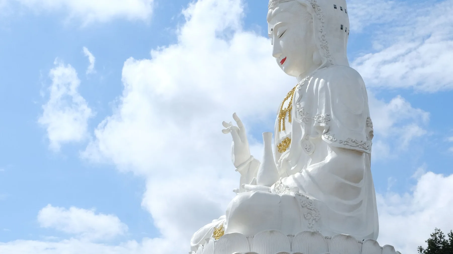 Estatua de Buda blanco entre vegetación, con el cielo azul de fondo