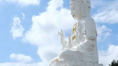 Estatua de Buda blanco entre vegetación, con el cielo azul de fondo
