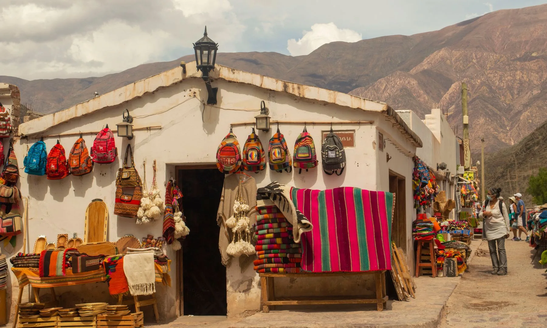Textiles coloridos y artesanías en un puesto del mercado de Purmamarca, con el cerro multicolor de fondo