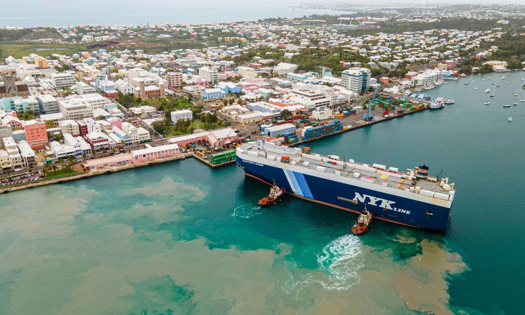 Aerial perspective of a cargo ship docking in Bermuda's vibrant port area.