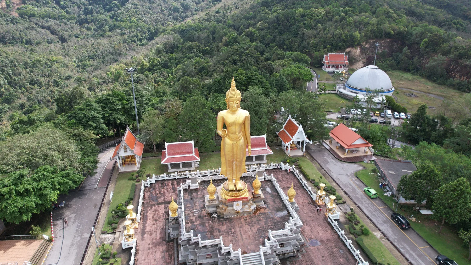 Vista aérea de una gran estatua dorada de Buda en un parque ceremonial rodeado de bosque, en Amnat Charoen, Tailandia