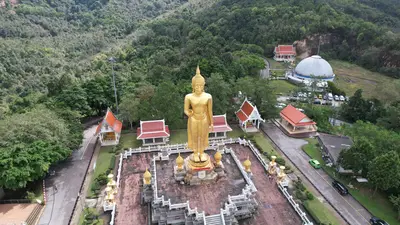 Vista aérea de una gran estatua dorada de Buda en un parque ceremonial rodeado de bosque, en Amnat Charoen, Tailandia