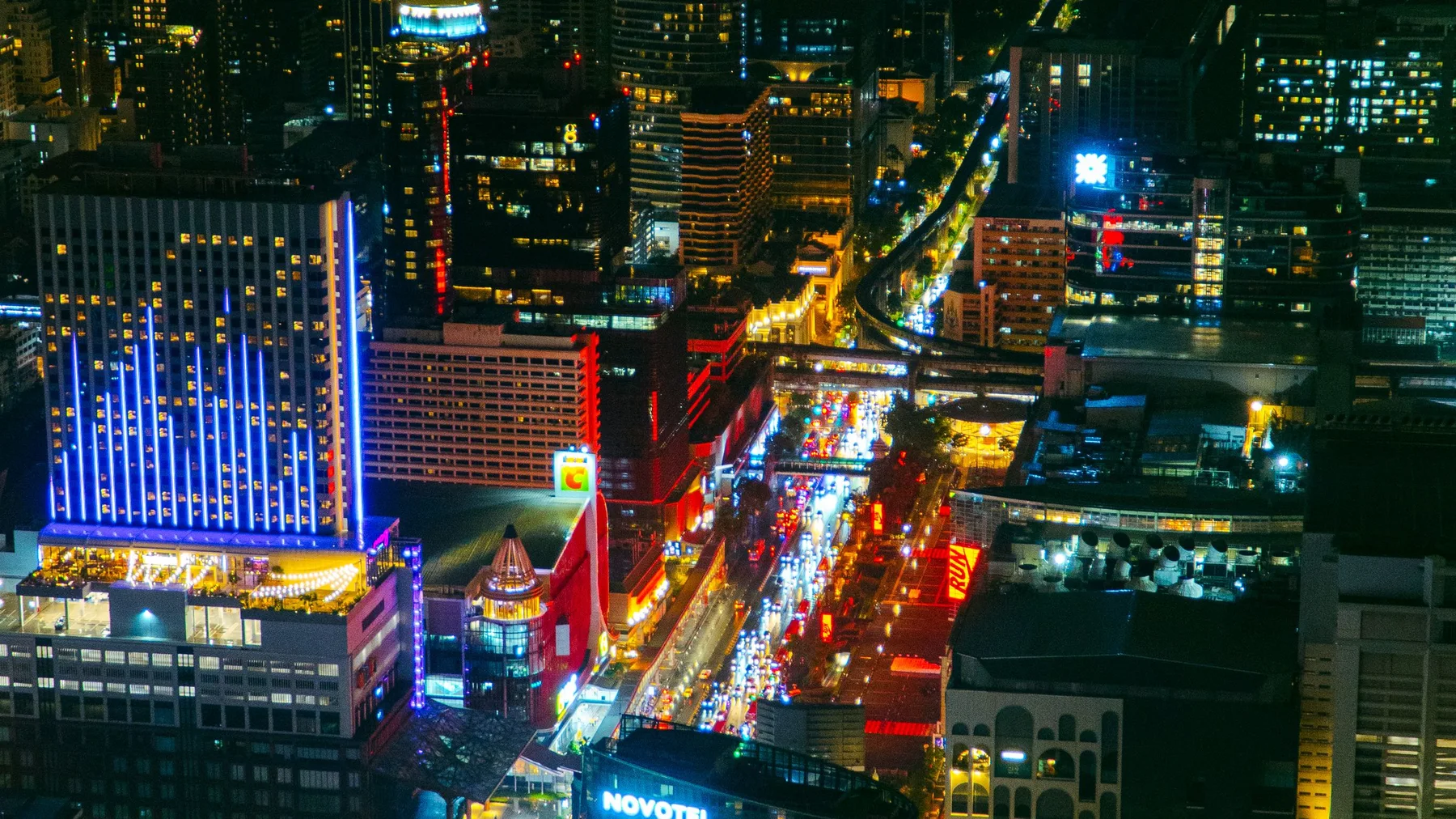 Vibrant nighttime aerial view of Bangkok's skyline with illuminated skyscrapers and bustling streets.