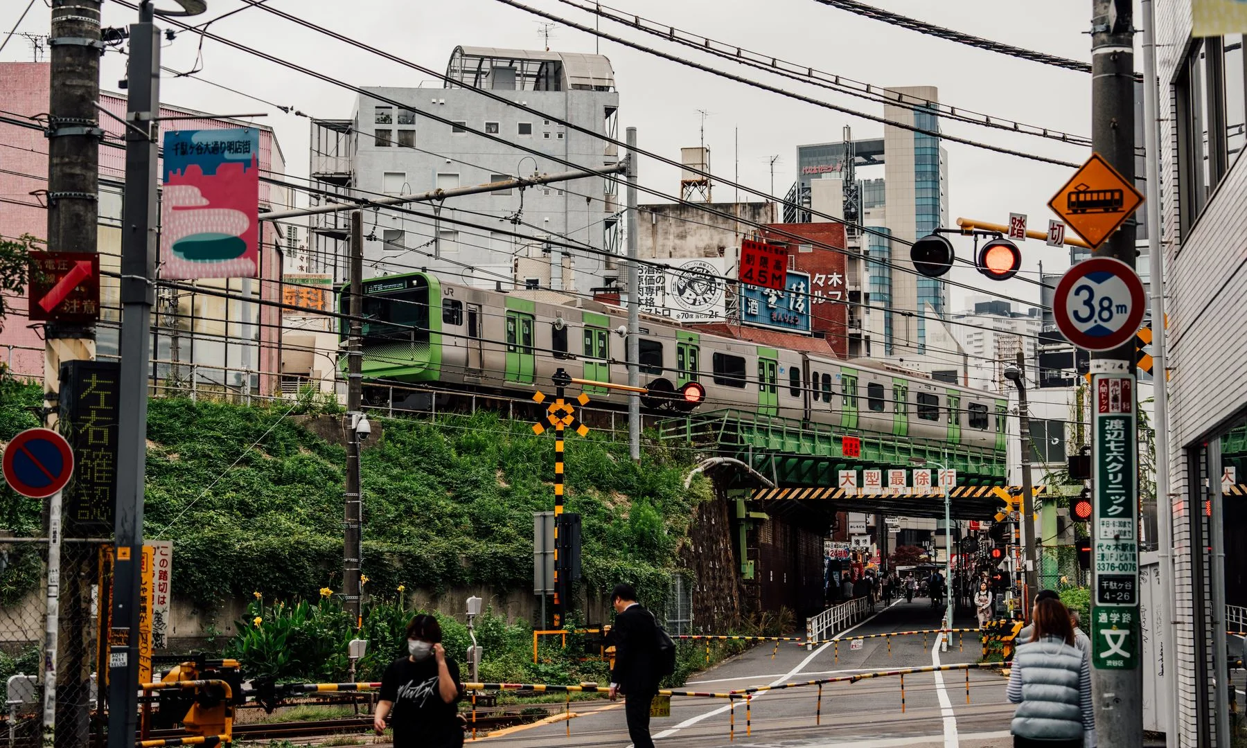 Calle urbana concurrida en Tokio con un tren elevado pasando sobre peatones