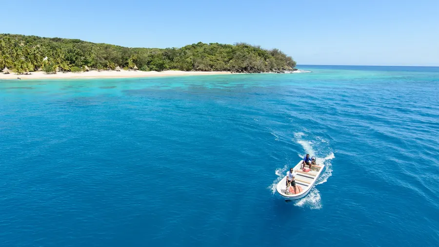 Vista aérea de una isla tropical en Fiyi, rodeada de mar azul y con una lancha a motor navegando