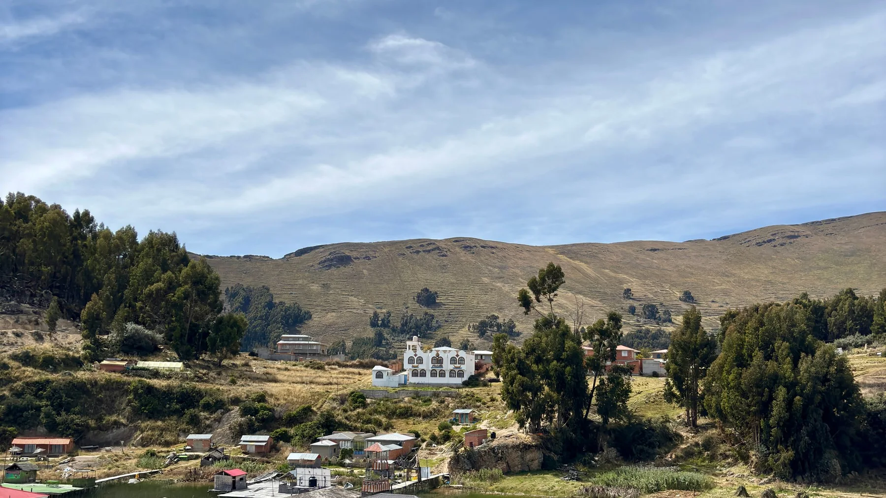 Tranquil scene of floating houses on Lake Titicaca in Copacabana, Bolivia, surrounded by hills and trees.