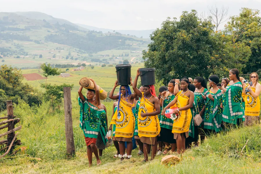 Grupo de personas espera entrar a un hogar para una ceremonia tradicional de boda en Esuatini, con regalos y cantos