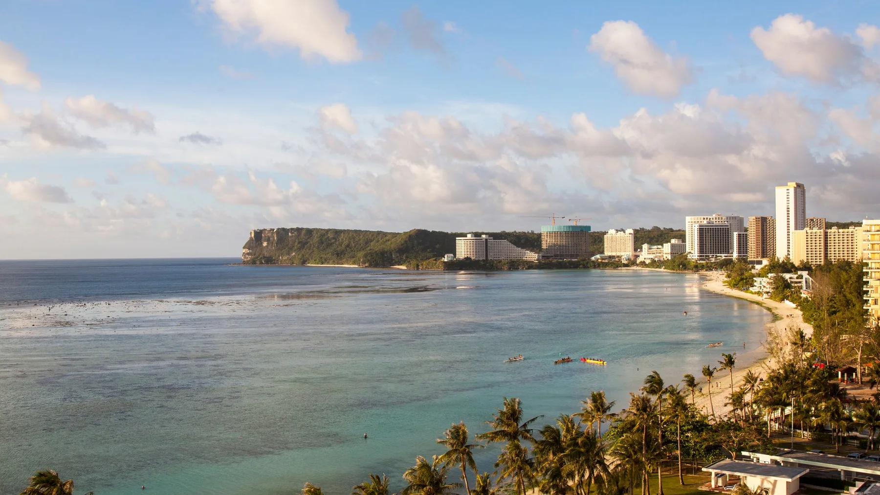 Vista aérea de una playa tropical y el perfil urbano de Guam, con la costa y edificios modernos