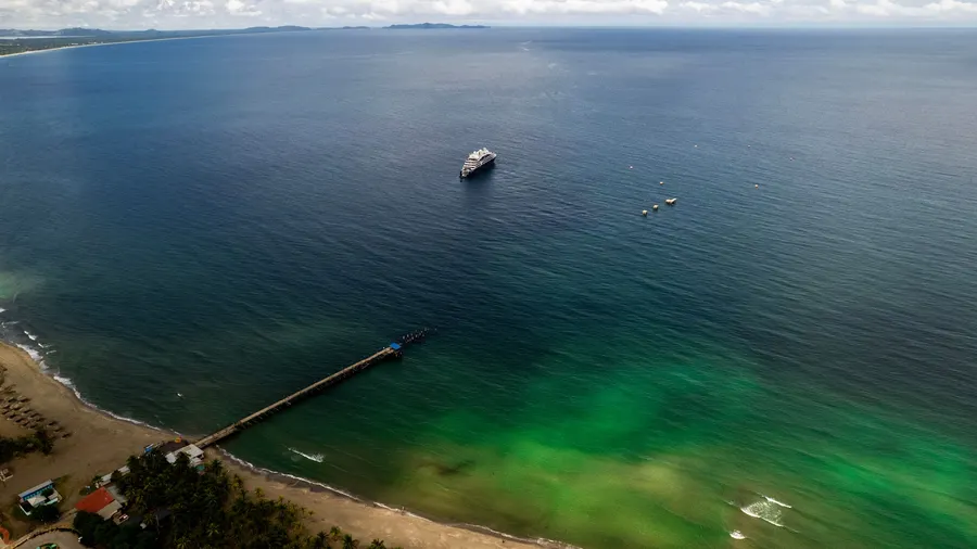 Vista aérea de la playa de Tela, Honduras, con un muelle y un barco sobre aguas de color intenso