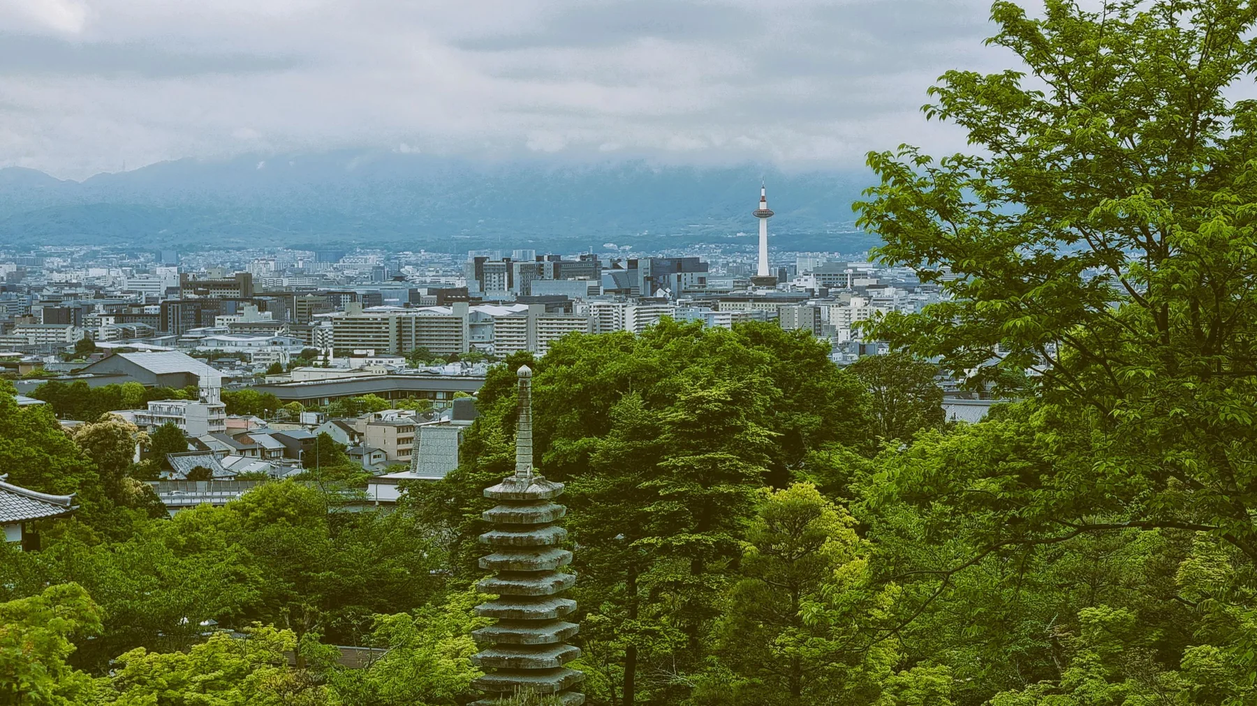 Scenic cityscape view from a pagoda in Kyoto with lush greenery and Kyoto Tower.