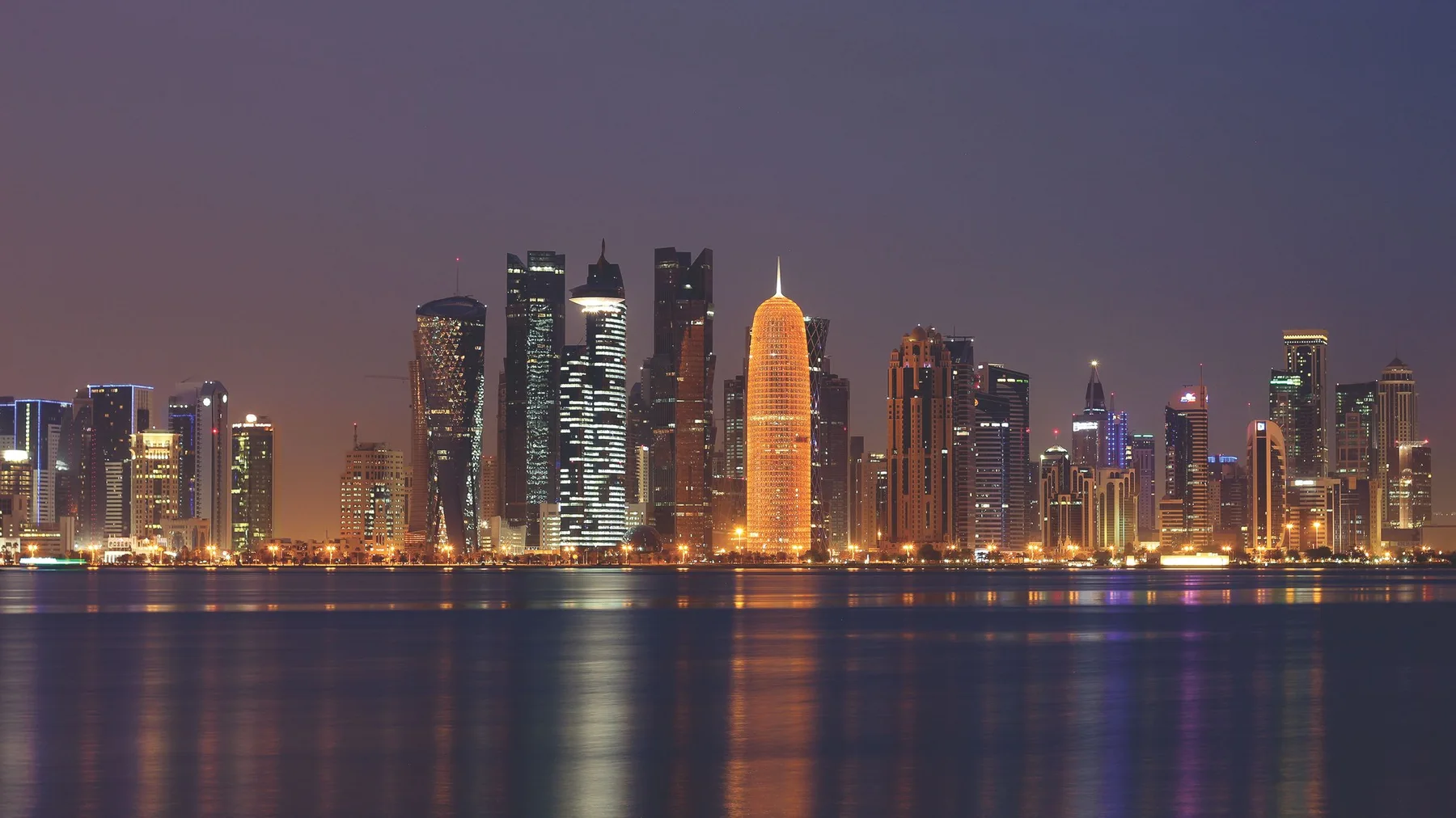 Panorámica nocturna de Doha, Catar, con rascacielos iluminados reflejados en el agua