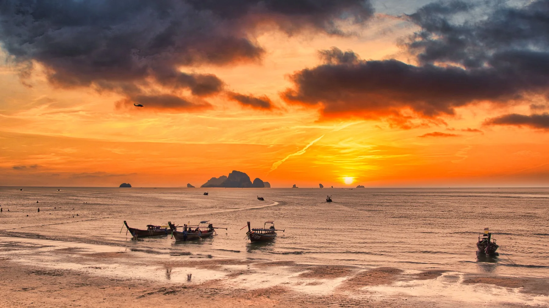 Golden sunset over Krabi beach with traditional boats and dramatic clouds.