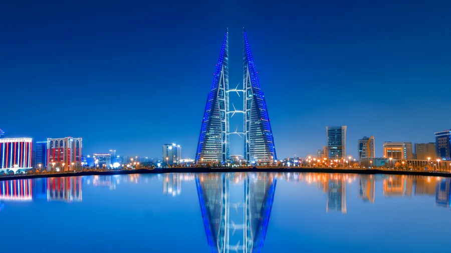 Vista nocturna del Bahrain World Trade Center con reflejos en el agua y el skyline moderno de Manama
