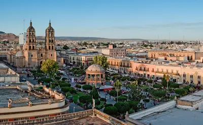 Plaza principal de Victoria de Durango con árboles, bancas y edificios históricos alrededor
