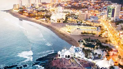 Vista aérea de la costa iluminada de Mazatlán al atardecer, con la ciudad y el litoral