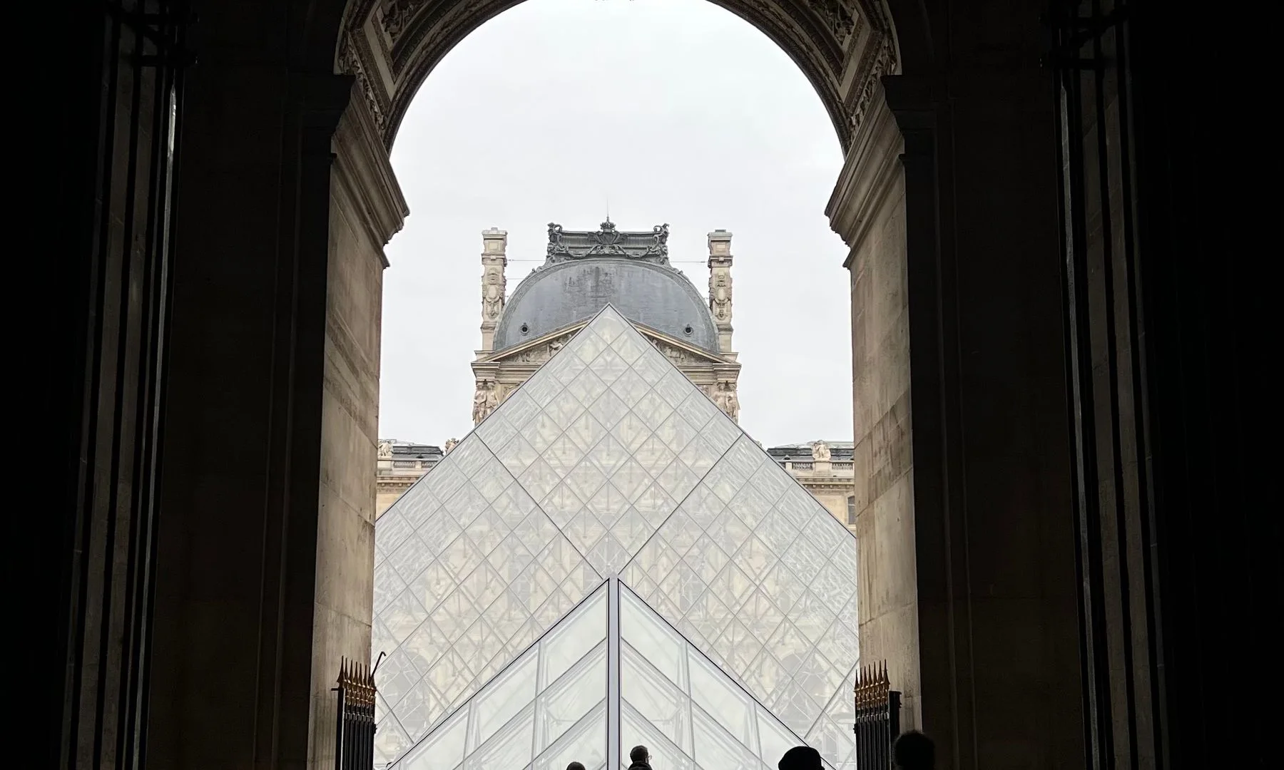 Personas en silueta frente al acceso del Museo del Louvre con la pirámide de vidrio, en París, Francia