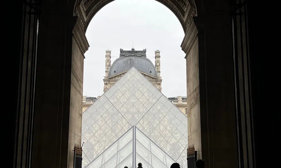 Personas en silueta frente al acceso del Museo del Louvre con la pirámide de vidrio, en París, Francia