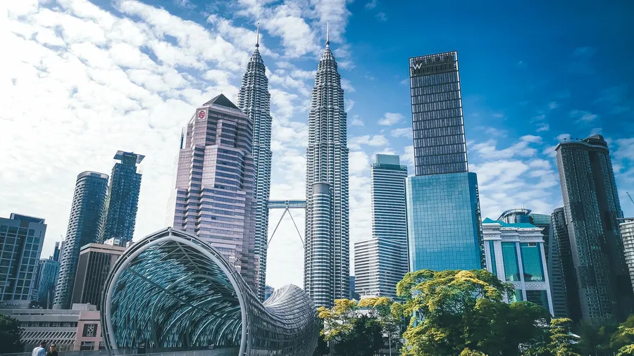 Panorama de Kuala Lumpur con las Torres Petronas entre rascacielos de vidrio y una pasarela peatonal futurista