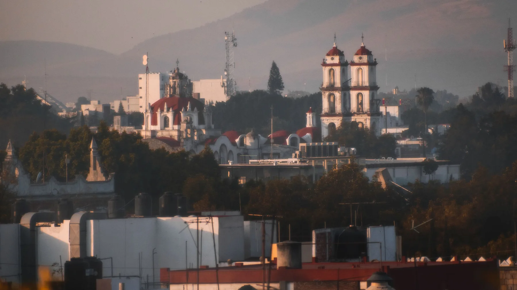 A picturesque view of Puebla de Zaragoza with iconic architecture and distant hills during sunset.