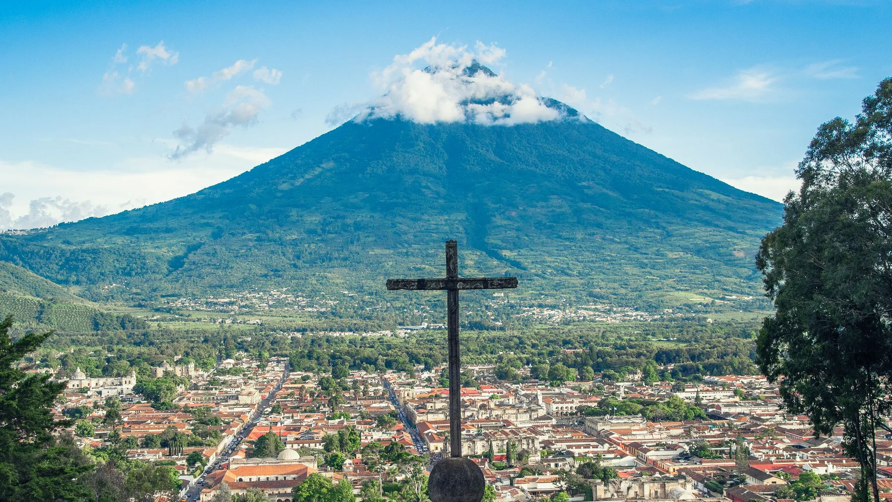 Vista panorámica de Antigua Guatemala con el Volcán de Agua al fondo y una cruz en primer plano