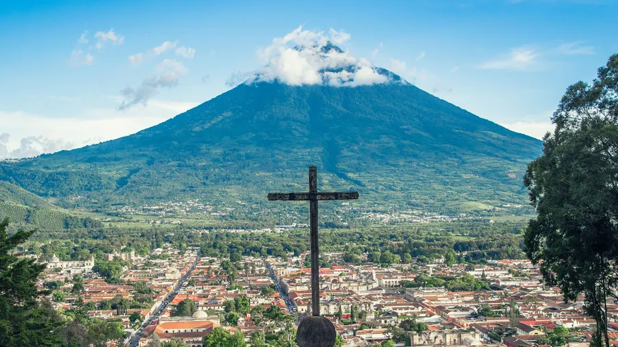 Vista panorámica de Antigua Guatemala con el Volcán de Agua al fondo y una cruz en primer plano
