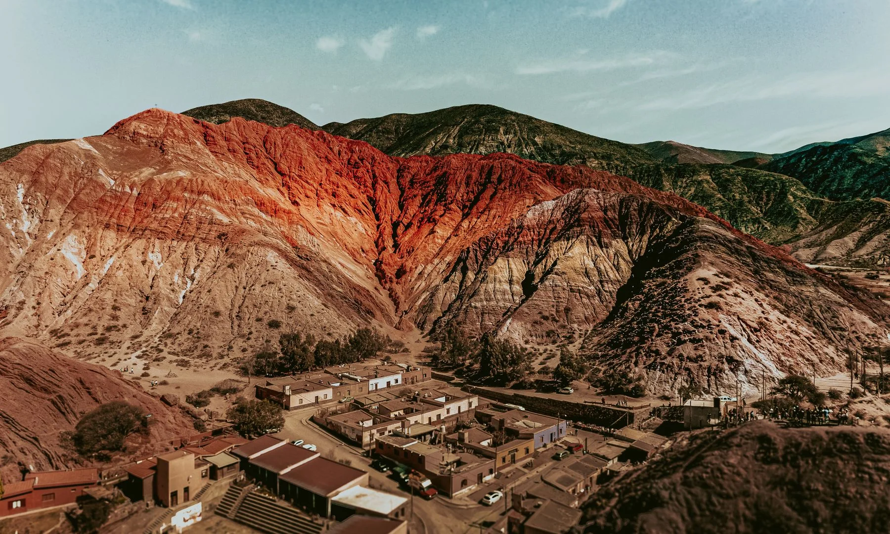 Vista aérea del Cerro de los Siete Colores en Purmamarca, con sus franjas ocres, rojizas, verdes y violáceas junto al pueblo
